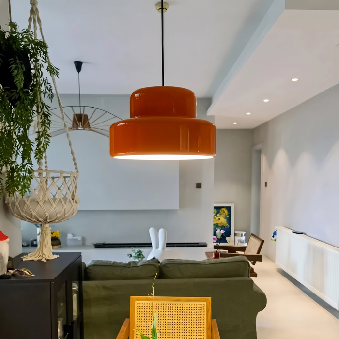 A pair of Sunna orange pendant lights lit over a kitchen island in an open-plan living room with a green sofa and cane chairs