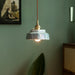 Pendant light with decorative shade hanging against a green wall.